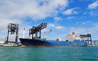 Cargo ship at Miami harbor with crane and blue sky over sea.